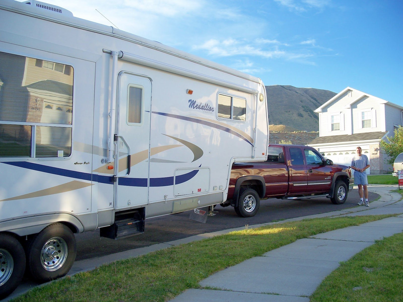 RV Being Pulled by Truck in Neighborhood with Mountainous Backdrop